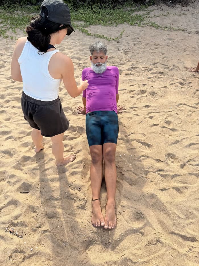 Rotem coaching a seated client through a core brace on the beach