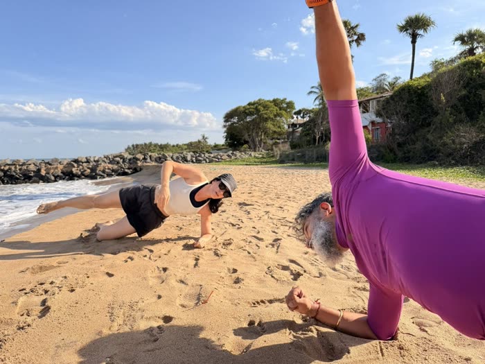 Wide beach view of Rotem and a client holding side planks